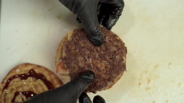 Chef preparing a big beef burger with full trimmings, grilled bacon and cheese placing a toasted bun.