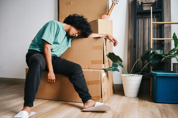 Asian man sitting near pile of cardboard boxes tired after moving house 