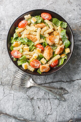 Delicious Caesar salad pasta with chicken, romaine lettuce, parmesan, tomatoes and croutons close-up in a bowl on the table. Vertical top view from above