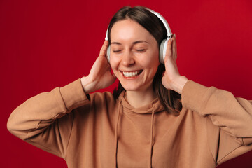 Wide smiling woman wearing white headphones enjoys the music she is listening.