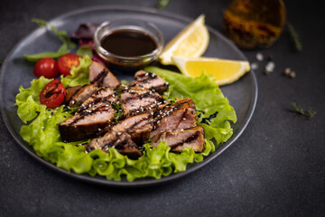 sliced pieces of Organic grilled Tuna Steak on black ceramic serving dish with salad on a table
