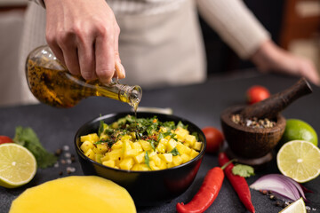 Cooking mango salsa - woman chef pouring cooking olive oil onto sliced chopped ingredients in a...