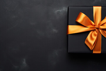 Top view photo of black giftbox with orange satin ribbon bow on isolated black background with copyspace