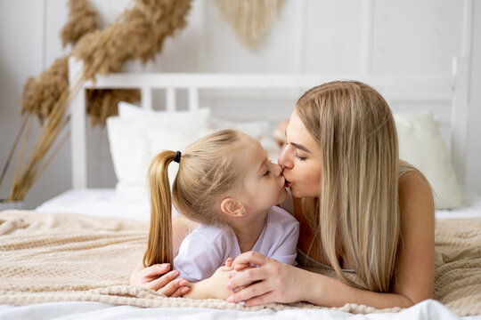mom and daughter play, hug and kiss at home on the bed, lifestyle, tender relationship of a young mother and child, happy family and motherhood