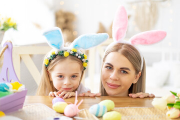 Obraz na płótnie Canvas easter, mom and little daughter with bunny ears on their head are preparing for the holiday by having fun playing and spending time together, colorful eggs, lifestyle,