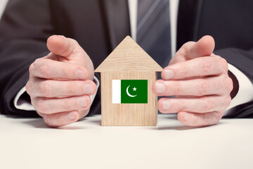 Businessman hand holding wooden home model with Pakistani flag. insurance and property concepts