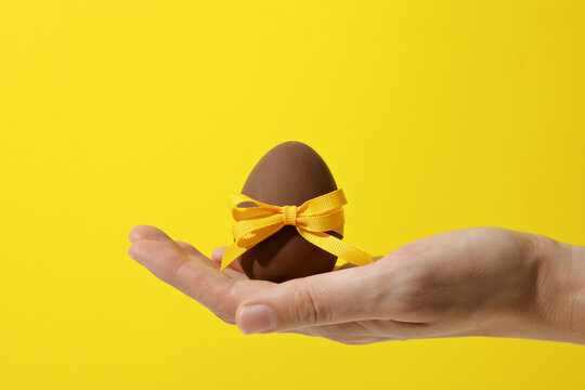 Chocolate egg in hand on yellow background