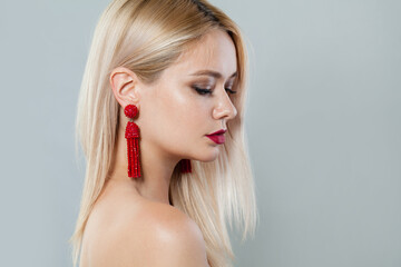 Nice fashion model woman with blonde hair wears big red color earrings. Fashionable lady with...