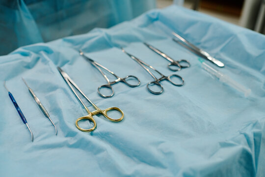 Set of sterile steel medical tools for carrying out surgical operation lying on blue napkin on push cart or table prepared for procedure