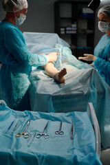 Operating tools on blue napkin and surgeon with female assistant in medical scrubs, gloves and masks surrounding patient