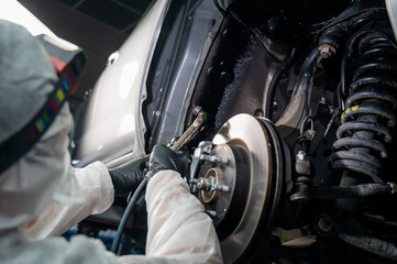 An auto mechanic applies anti-corrosion mastic to the underbody of a car.