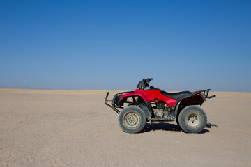 Red quad bike stands on the sand against the Arabian desert skyline in Egypt