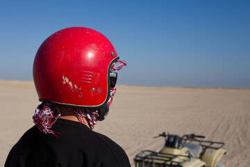 Man in helmet next to an ATV in desert on a sunny day during a safari, close up photo