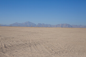 Desert skyline with clear sky and tire tracks in the sand and mountains in the distance