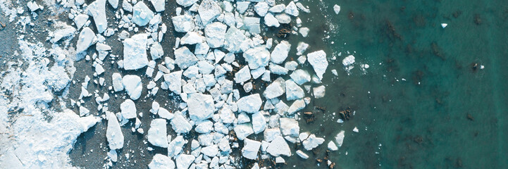Top view of the white ice floes on the shore and in the blue sea water. Aerial view of melting ice on the sea coast. Climate change in the Arctic. Northern nature. Beautiful wide panoramic background.