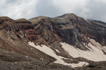 Majestic mountain landscape. The rim of a volcanic crater. View of the rock layers on the inner slope of the volcano's crater. Nature of the Russian Far East. Gorely volcano, Kamchatka Krai, Russia.