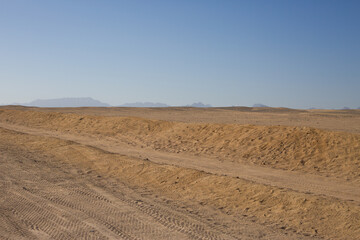 Fototapeta na wymiar Desert horizon on hot day against clear sky. Tire tracks on the sand in the Arabian desert on the way to safari road