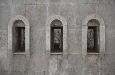 3 three arched Classic windows in granite exterior wall.  small wooden arched windows protected.  windows set into a solid wall built of granite blocks, in front. orthodox church in Georgia.