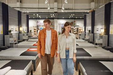 Young man and woman couple looking for new bed at modern furniture shop