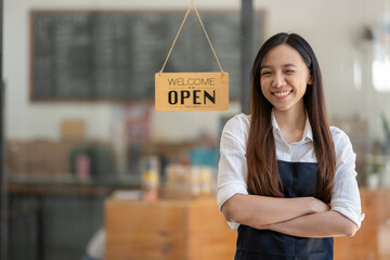 A confident and smiling Asian female cafe owner stands proudly with crossed arms behind a 'Welcome...