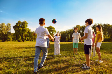 Happy joyful children boys and girls playing with a ball on a green grass in the park outdoors. Kids standing in a circle on the lawn in the garden catching ball and having fun in summer camp.