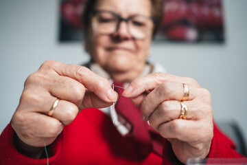 concentrated seamstress with glasses threading sewing thread into needle