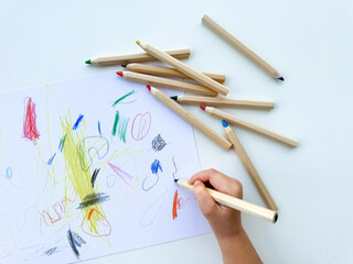 small child draws with colored pencils on paper on white table.