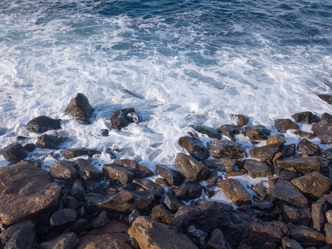 Rocky beach in the south of Tenerife with waves crashing on the beach of volcanic stones. You can see water pollution, due to landfills contaminating the water.