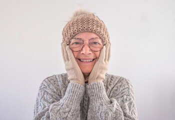 Portrait of smiling senior woman in gray sweater with glasses cap and gloves looking at camera, isolated on white background. Winter concept