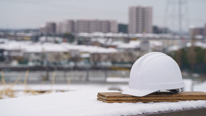 ヘルメットと雪の積もる冬の街並み｜冬の建設業イメージ