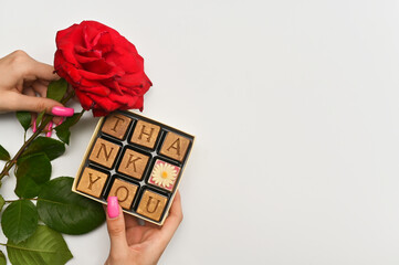 a rose and chocolates in a woman's hand. on a white background. Thank you for the concept
