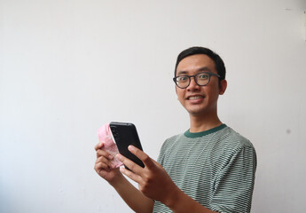 Adult Asian man with glasses showing happy face expression while holding mobile phone and paper money, isolated background