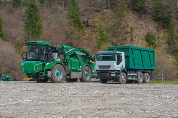 Fototapeta premium An industrial wood chipper with off-road capability and a truck on a logging site near the mountain village of Forni Avoltri in Carnia, Udine Province, Friuli-Venezia Giulia, north east Italy