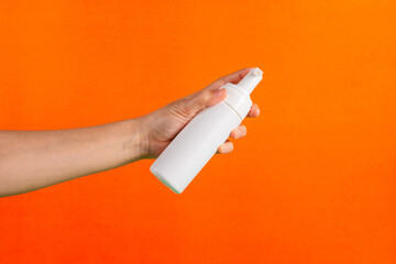 Cosmetic white bottle. Womens cosmetic accessory and hand for makeup on orange background.