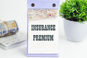 Business concept. text INSURANCE PREMIUM written on a desktop tear-off calendar on a white background, next to a calculator with a roll of banknotes with a flower out of focus in the background