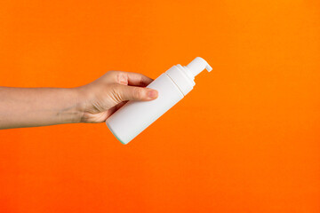Cosmetic white bottle. Womens cosmetic accessory and hand for makeup on orange background.