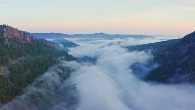 Aerial view of clouds in mountain valley. Scenery sunrise at Ural mountain. Flying over morning haze in a valley