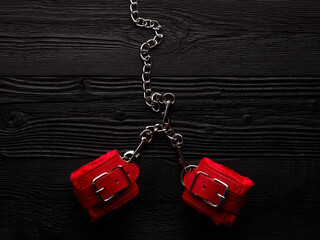 BDSM role play background with bright red handcuffs over black wooden backdrop