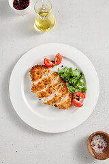 Crispy breaded chicken fillet served with fresh greens and tomato slices, suitable for restaurant menus and recipe blogs