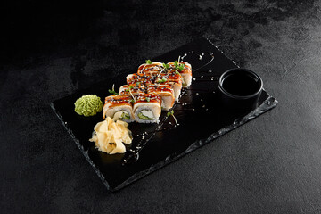 Canada roll with eel and unagi sauce, presented on a black slate with soy sauce and wasabi