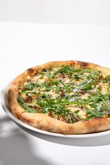 Italian pizza with cheese and mushrooms, adorned with arugula and cast in shadow on a white background