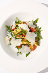 Top view of a salad with artichokes, tomatoes, and shaved Parmesan cheese on a white plate