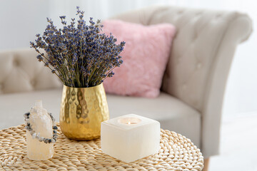 Selenite crystal candle holder and tower for good energy, dry lavender flower in vase in light color home living room, sofa with pink pillow on background.