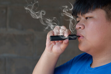 Young asian man smoking electronic cigarette on dark background. Close up.