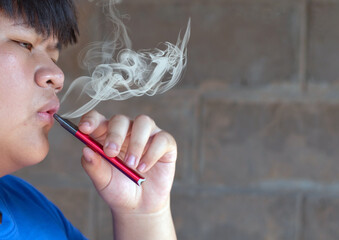 Young asian man smoking electronic cigarette on dark background. Close up.