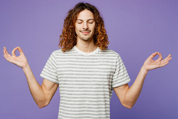 Young spiritual man wears grey striped t-shirt casual clothes hold spreading hands in yoga om aum gesture relax meditate try to calm down isolated on plain pastel purple background. Lifestyle concept.