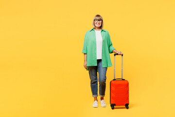 Full body traveler elderly woman wear green casual clothes hold suitcase bag isolated on plain yellow background. Tourist travel abroad in free spare time rest getaway Air flight trip journey concept