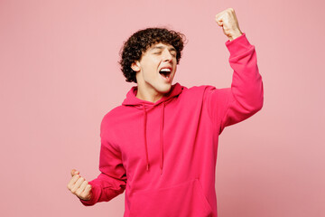 Young excited fun Caucasian man he wears hoody casual clothes doing winner gesture celebrate clenching fists say yes isolated on plain pastel light pink background studio portrait. Lifestyle concept.