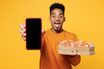 Young man in casual clothes hold italian pizza in cardboard flatbox use black screen mobile cell phone isolated on plain yellow background Proper nutrition healthy fast food unhealthy choice concept