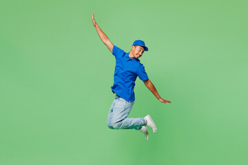 Full body side view delivery guy employee man he wears blue cap t-shirt uniform workwear work as dealer courier jump high with outstretched hands isolated on plain green background. Service concept.
